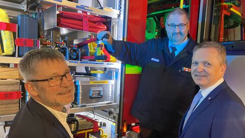 Drei Männer stehen vor einem Feuerwehrauto