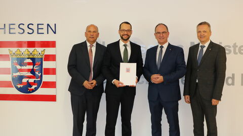 Mehrere Männer im Anzug stehen vor Wand. Auf Wand ist die Hessen-Marke zu sehen