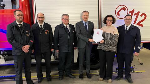 5 Männer und 1 Mann stehen vor einem Feuerwehrauto und halten einen Förderbescheid hoch