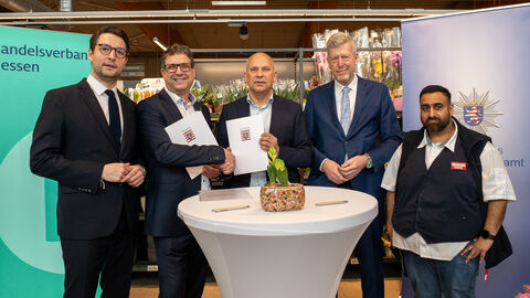 Innenminister Poseck und weitere Personen stehen um einen Stehtisch herum und halten die Kooperationsvereinbarung in Händen.