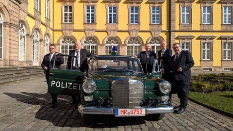 Fünf festlich gekleidete Herren stehen vor dem Residenzschloss neben einem Oldtimer Polizeiauto.