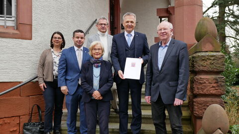 Sechs Männer und Frauen stehen versetzt auf einer Treppe vor einem Gebäude.
