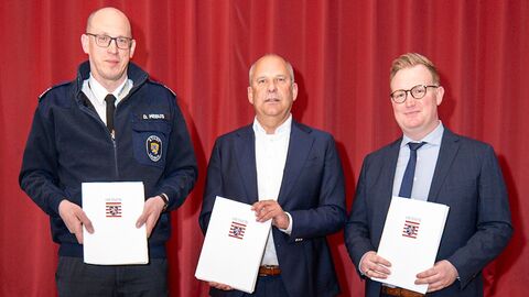 Innenminister Poseck und zwei weitere Personen stehen nebeneinander und halten Bescheide in den Händen.