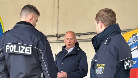 Innenminister Poseck steht vor zwei Polizisten und unterhält sich.
