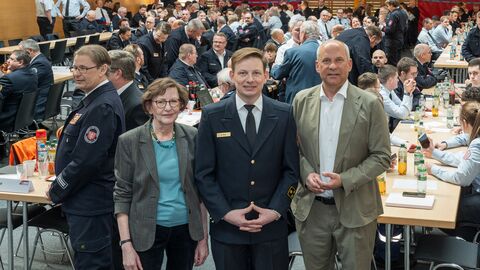 Stadträtin Annette Rinn, Innenminister Roman Poseck und der neue Chef der Frankfurter Feuerwehr Markus Röck schauen in die Kamera. Hinter ihnen sitzen zahlreiche uniformierte Personen in einem Saal.