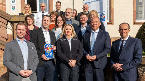 Innenminister Roman Poseck steht mit 15 weiteren Personen auf den Treppen des Rathauses - im Hintergrund ein Plakat zur Initiative Kompass Hessen