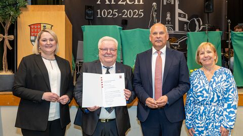 Bürgermeisterin Dana Hauke, Ortsvorsteher Klaus-Dieter Rucht, Kommunalminister Roman Poseck und Andrea Vogt stehen vor einem Plakat „Arzell 1025-2025“. Rucht hält eine Urkunde in die Kamera.