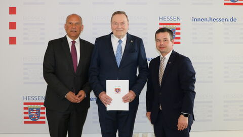 Drei Personen stehen zusammen, die Person in der Mitte hält einen Bescheid in Händen.