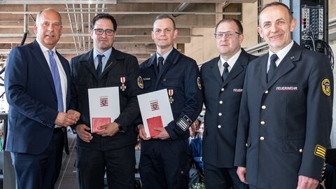 Innenminister Poseck und weitere Personen in Feuerwehr-Uniform stehen zusammen und halten Bescheide in Händen.
