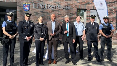 Innenminister Poseck und weitere Personen, teils in Polizeiuniform, stehen vor einem Gebäude mit der Aufschrift "1. Polizeirevier".
