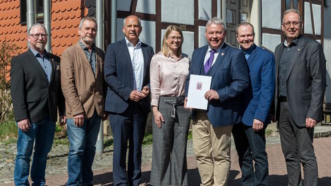 Innenminister Poseck steht mit weiteren Personen vor einem Gebäude und überreicht einen Zuwendungsbescheid.