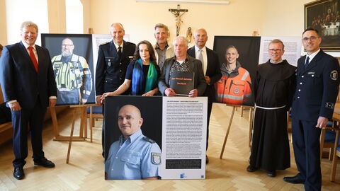 Mehrere Personen stehen in einem Raum, zwischen Ihnen Portraits von Einsatzkräften.