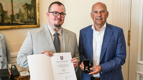 Innenminister Roman Poseck mit Matthias Reitz  - Herr Reitz hält eine Urkunde in der Hand