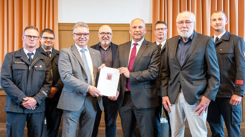 Acht Männer stehen nebeneinander. Die mittleren drei halten eine ausgedruckte Urkunde in Papierform hoch.