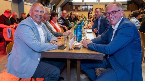 Mehrere Personen sitzen an langen Tafel und lachen in Kamera.