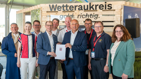 Zehn Männer und Frauen stehen nebeneinander und halten eine Urkunde hoch.