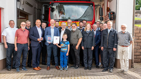 Roman Poseck steht mit einer Gruppe von Menschen vor einer Garage, in welcher ein Feuerwehrwagen steht. 