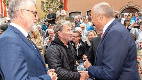 Zwei Männer geben sich die Hand. Im Hintergrund sieht man Publikum.