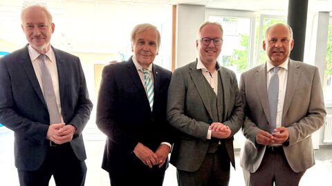 Vier Personen stehen zusammen zum Foto aufgestellt in einem Raum und lächeln in die Kamera.