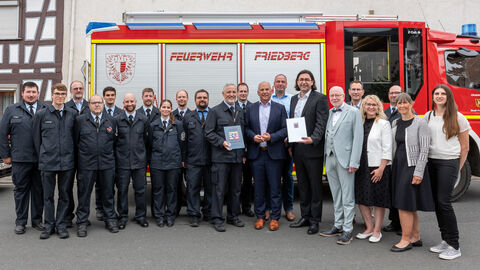 Roman Poseck steht mit einer Gruppe von teils uniformierten Menschen vor einem Feuerwehrwagen.