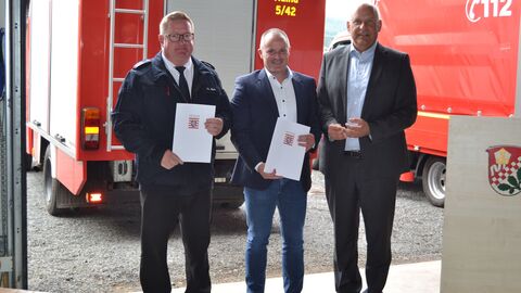 Innenminister Roman Poseck gemeinsam mit Bürgermeister Alexander Köhler und dem Gemeindebrandinspektor Thomas Bahr vor Einsatzfahrzeugen
