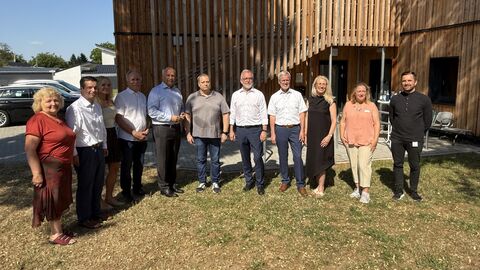 Elf Personen stehen auf einer Wiese und hinter ihnen ist ein Gebäude.