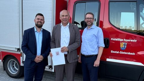 Drei Personen stehen vor einem Feuerwehrauto.