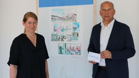 Eine Frau und ein Mann stehen vor einer Wand auf der ein Cartoon abgebildet ist