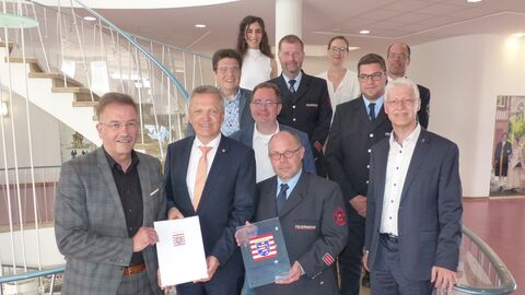 Mehrere Personen stehen auf einer Treppe. Zwei Personen halten eine Urkunde und eine Auszeichnung in der Hand.