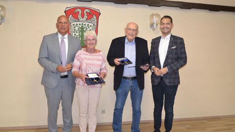 Vier Personen stehen nebeneinander. Die mittleren Personen halten jeweils einen Orden in der Hand.