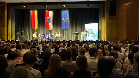 Vier Menschen sitzen auf einer Bühne. Davor sind Besucher von hinten zu sehen, die zuhören.