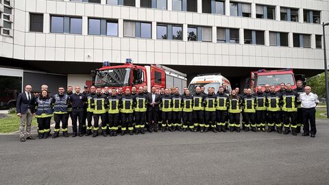 Eine größere Gruppe Einsatzkräfte stehen aufgereiht vor einem Gebäude und Einsatzfahrzeugen.