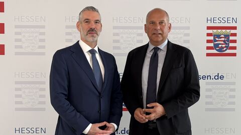 Von links nach rechts: Daniel Neumann und Roman Poseck stehen vor einem Plakat mit dem Logo des Innenministeriums.