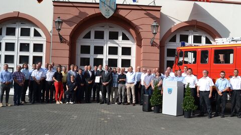 Innenminister Roman Poseck steht zusammen mit einer großen Gruppe von Menschen vor einem historischen Gebäude, neben ihnen ein Feuerwehrfahrzeug