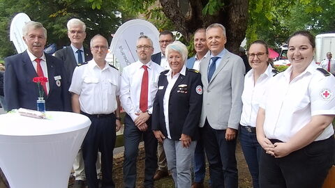 Innenstaatssekretär Martin Rößler mit Personen des DRKs stehen auf einer Wiese in einer Reihe. 