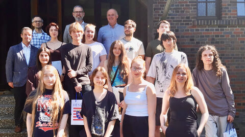 Eine Gruppe von Schülern steht mit dem Landesbeauftragten Hofmeister auf Treppenstufen. Die Schüler halten Tüten mit Hessen Logo in der Hand