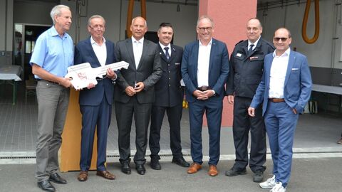 Roman Poseck steht in einer Reihe mit sechs weiteren Männern, einige tragen elegante Feuerwehruniformen.