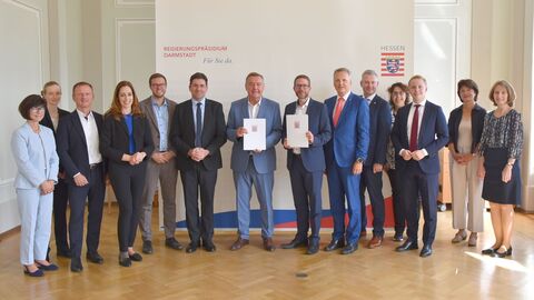Innenstaatssekretär steht mit einer Gruppe von Personen vor einem Poster mit der Aufschrift "Regierungspräsidium Darmstadt"