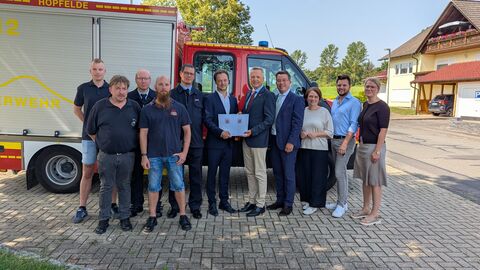 Eine Personengruppe steht zur Bescheidübergabe vor einem Feuerwehrfahrzeug.