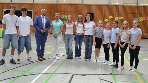 Zwei Erwachsene stehen gemeinsam mit mehreren Schülerinnen und Schülern in Turnhalle