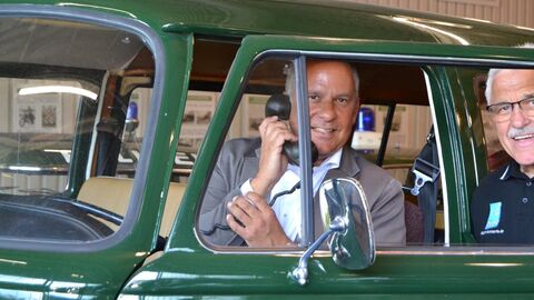 Roman Poseck sitzt in einem grünen Oldtimer Auto und hält sich einen Telefonhörer ans Ohr