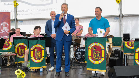 Martin Rößler steht auf einer Bühne - im Hintergrund sitzt ein Musikverein