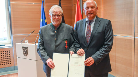 Innenminister Roman Poseck steht neben Heinz Gerlach, beide halten gemeinsam ein Schriftstück in den Händen.