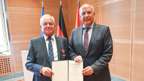 nnenminister Roman Poseck steht neben Theodor Kohlmann und halten zusammen ein Schriftstück in den Händen