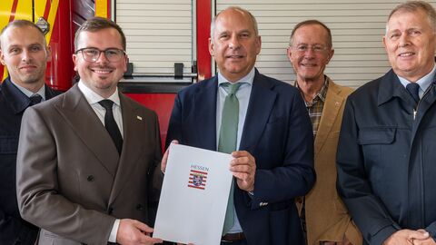 Fünf Männer stehen vor einem Feuerwehrfahrzeug. Zwei halten einen Bescheid in den Händen.