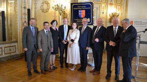 Mehrere Männer und zwei Frauen stehen zusammen und lächeln in Kamera.