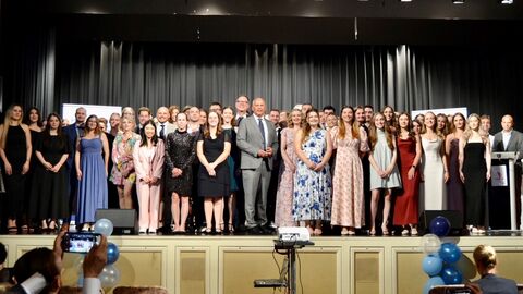 Absolventinnen und Absolventen stehen gemeinsam mit dem Minister auf einer Bühne