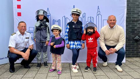 Der Innenminister mit einem Polizisten und vier Kindern mit Polizeimützen und -helmen.