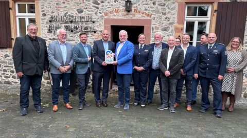 Roman Poseck steht mit circa 10 weiteren Personen vor einem historischen Gebäude und hält ein Schild mit der Aufschrift "Kompass" in den Händen.