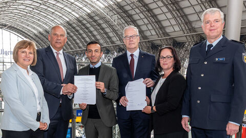 Innenminister Poseck steht mit weiteren Personen im Frankfurter Hauptbahnhof und hält Schreibstücke in die Kamera